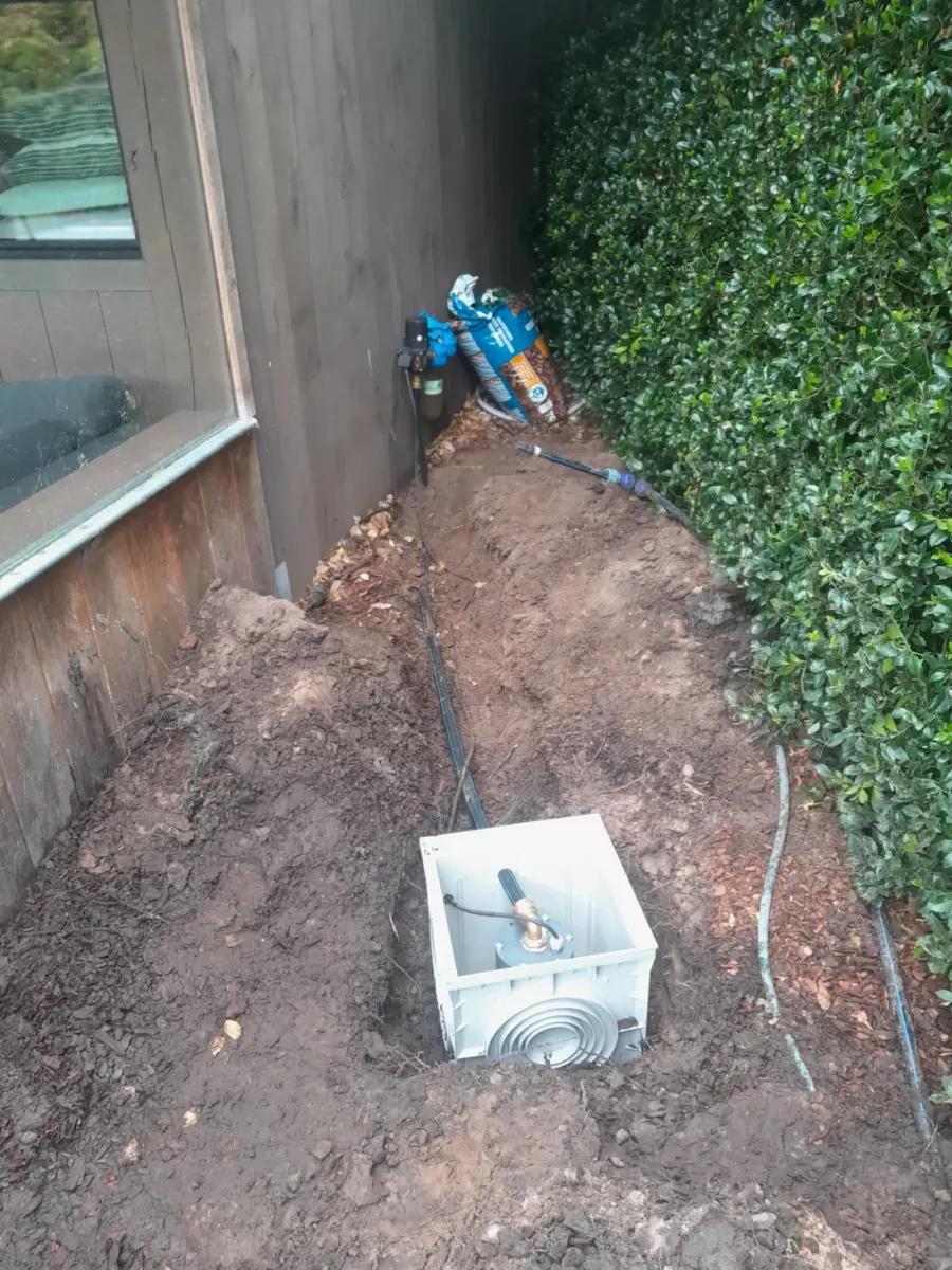 Bovenaanzicht van een uitgegraven sleuf langs een gazon, met de leiding klaar om te leggen.