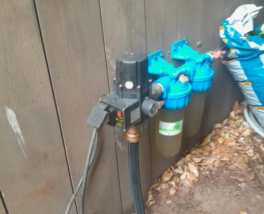 Close-up van een filterinstallatie met drukschakelaar en twee turquoise filterhuizen op de watertoevoer.